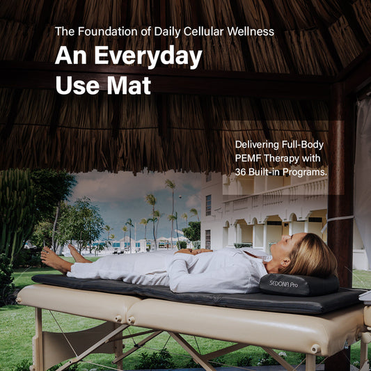 Promotional graphic for the PRO PEMF MAT, showing a woman lying on a massage-style therapy table under a thatched roof outdoors. Large text reads 'The Foundation of Daily Cellular Wellness' and 'An Everyday Use Mat,' with smaller text about PEMF therapy programs.